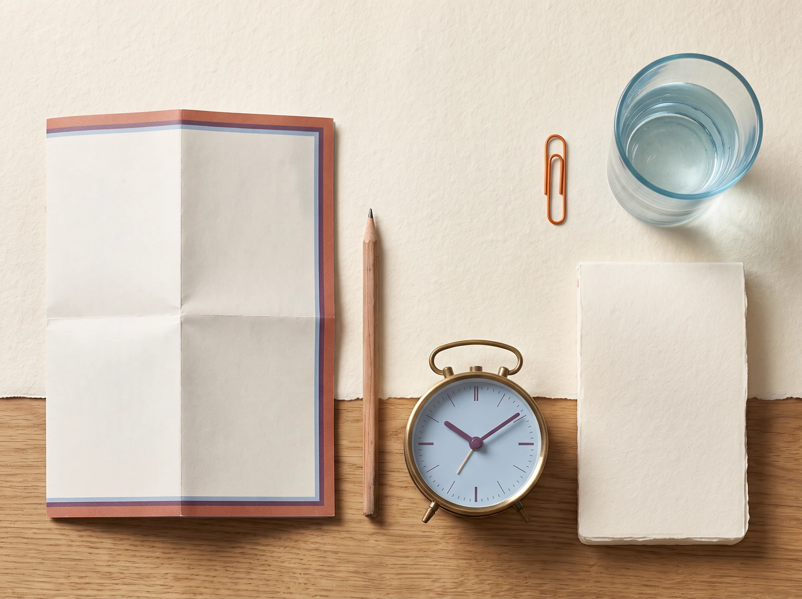 Open blank notebook, pencil, paper clip and small clock on a table